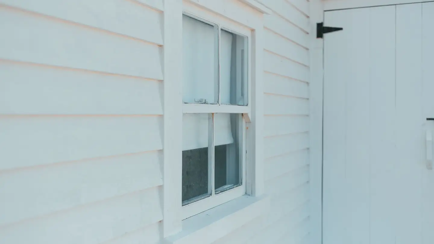 Close-up of white-painted wooden siding with a window and door trim.